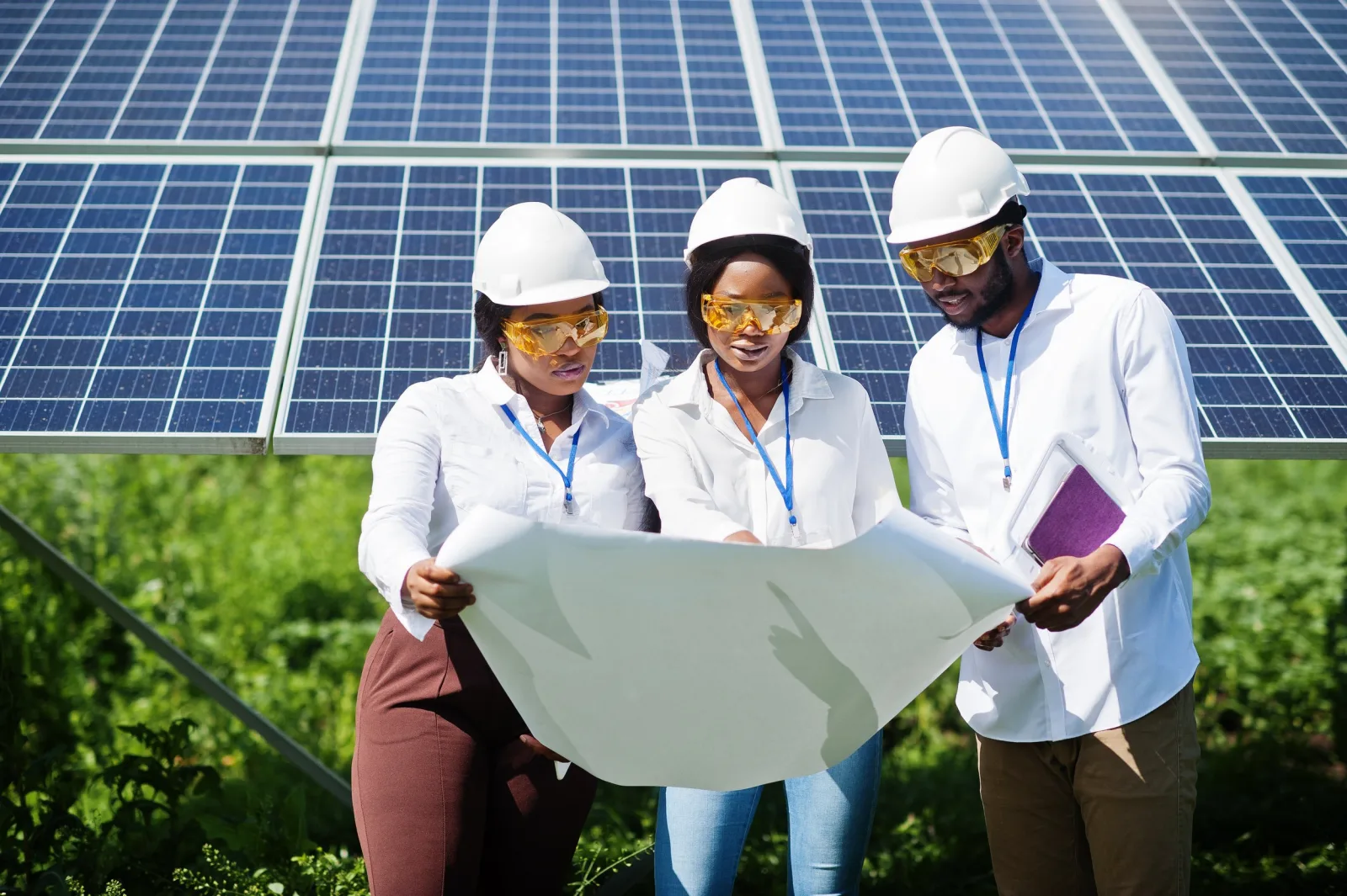 Three solar professionals in hard hats reviewing plans beside a photovoltaic array