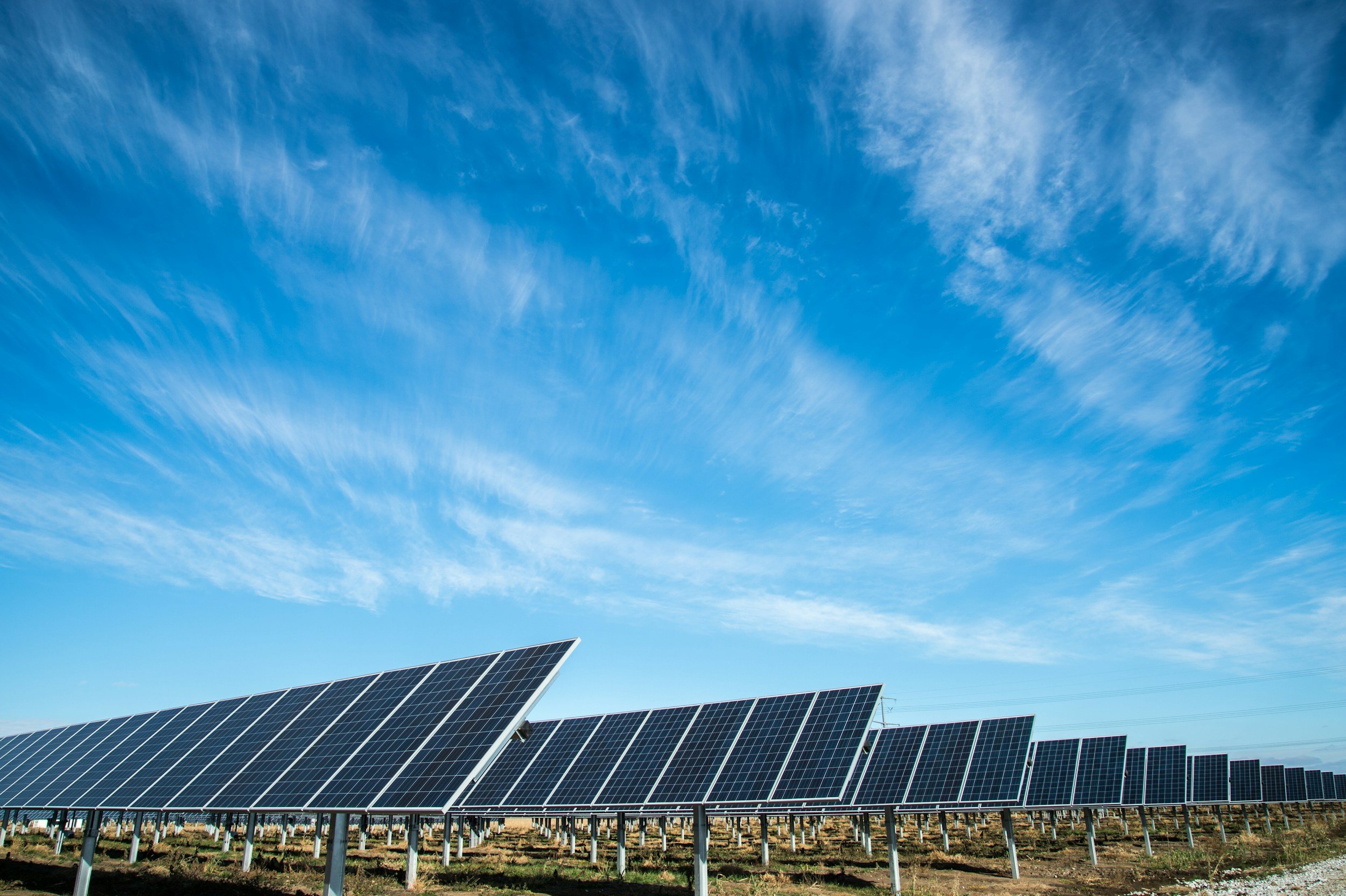 Rows of photovoltaic panels beneath a blue sky with wispy clouds