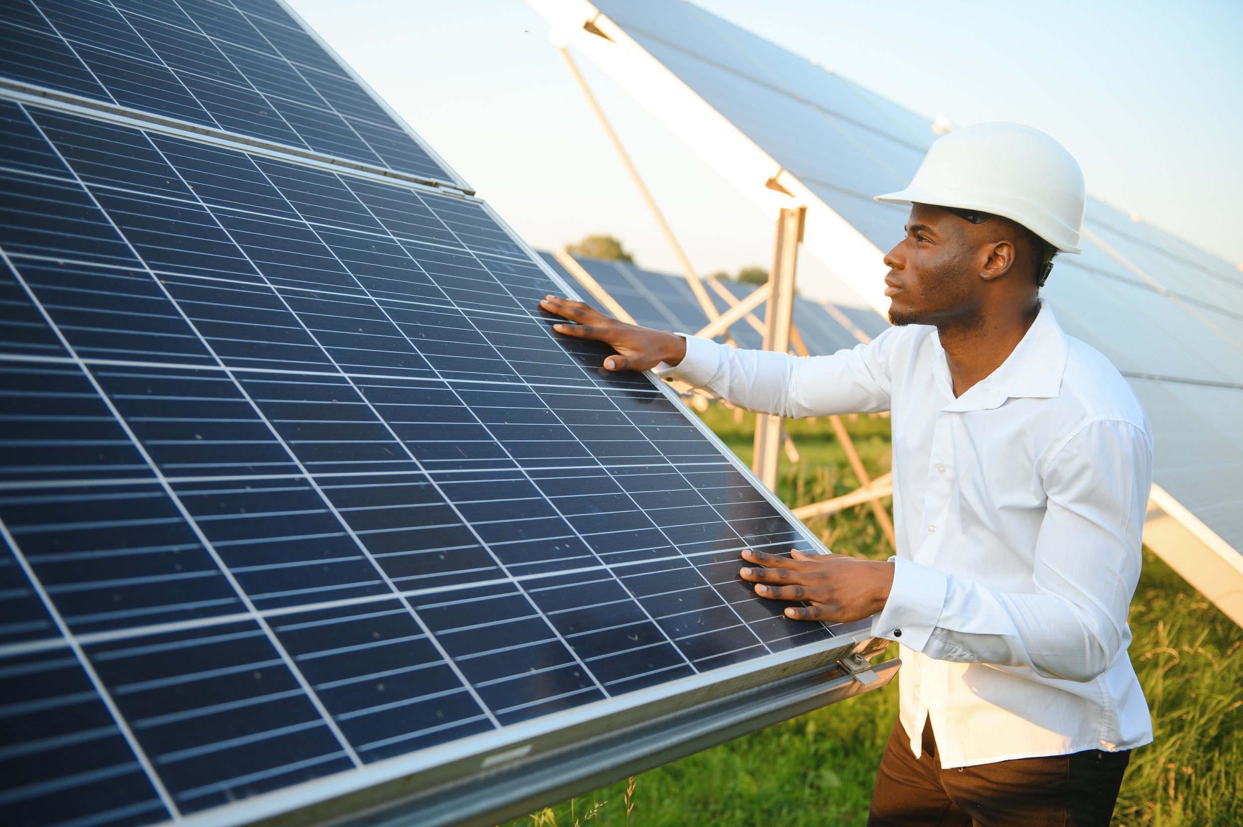 A solar technician in a hard hat inspecting a photovoltaic panel